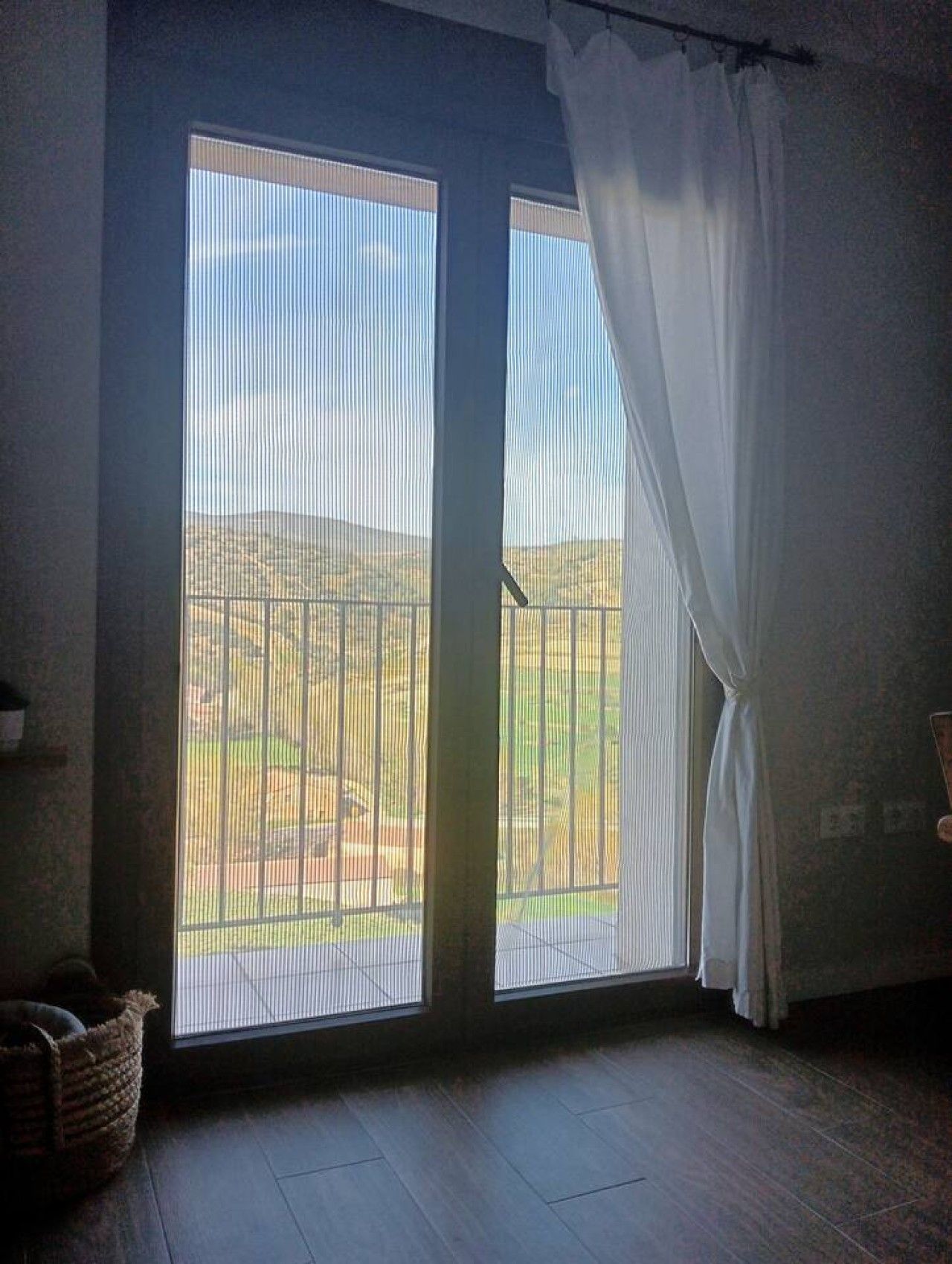 Ein Zimmer mit einem großen Fenster, einem dunklen Holzboden und einem Korb auf der linken Seite.