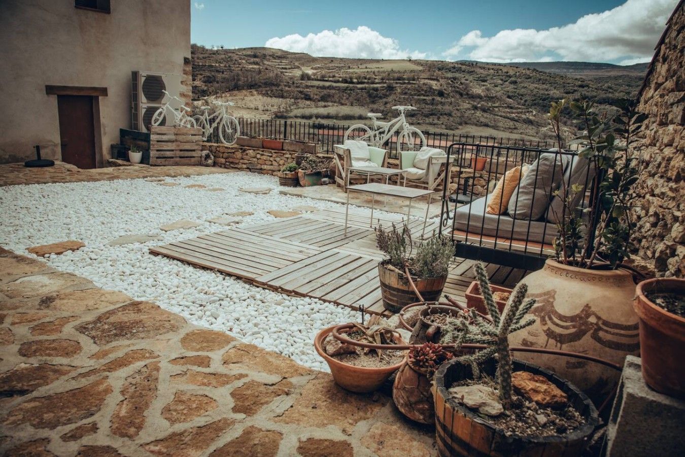 Eine Terrasse mit Steinboden, Pflanzkübeln, einer Holzterrasse und Blick auf eine hügelige Landschaft.
