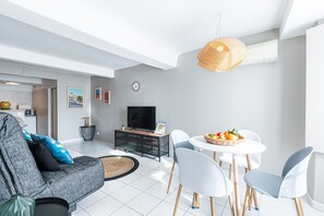 Ein modernes Wohnzimmer mit einer Couch, einem Esstisch mit Stühlen, einem Fernseher und einer an der Wand befestigten Uhr.