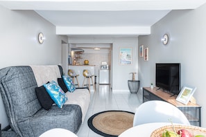 Een moderne woonkamer met een grijze bank, een flatscreentelevisie en een eethoek met een tafel en stoelen.