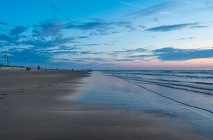 Una spiaggia con un mare calmo, cielo sereno e turbine eoliche all'orizzonte.