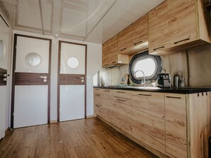 Cozinha compacta com armários de madeira, uma janela redonda sobre a pia e uma porta com uma janela circular.