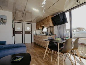 Cozinha moderna com armários de madeira, área de jantar com mesa e cadeiras, e uma janela grande com vista para um barco.