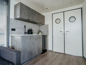 Cozinha compacta com armários cinza, forno embutido e máquina de café.