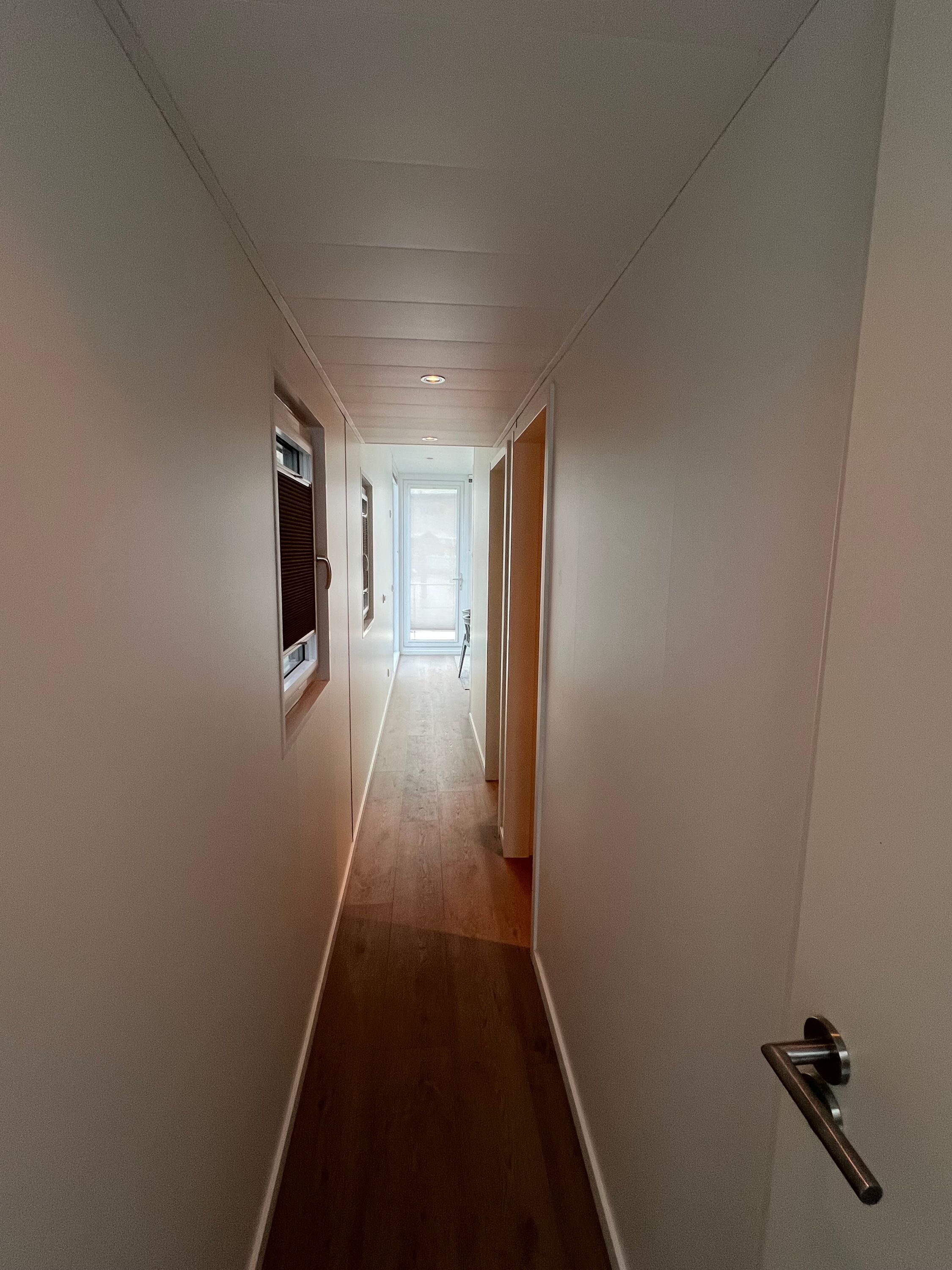 A narrow hallway with a wooden floor, white walls, and a door on the right.