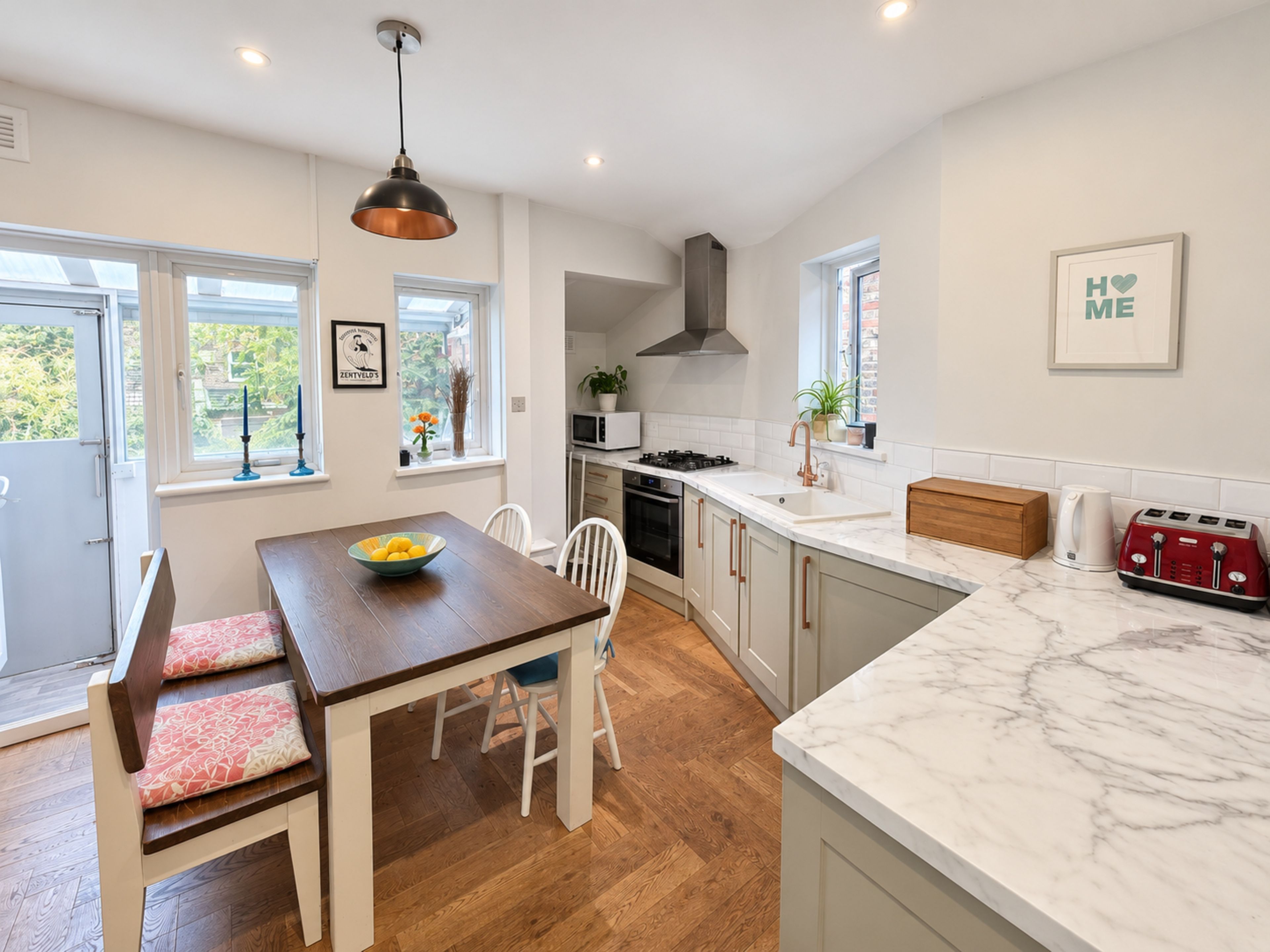 A modern kitchen with a wooden dining table, white chairs, and a marble countertop.