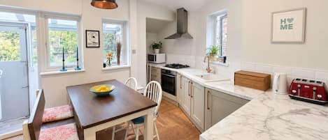 A modern kitchen with a wooden dining table, white chairs, and a marble countertop.