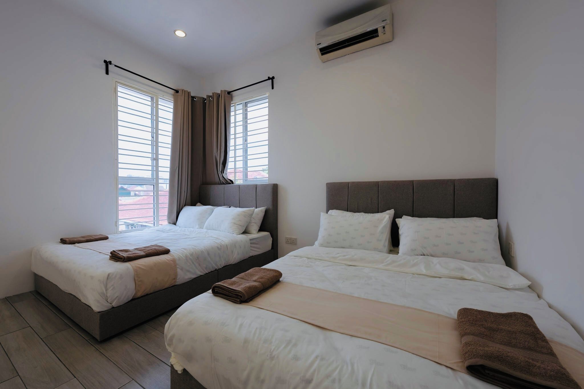 A hotel room with two beds, a window with blinds, an air conditioning unit, and a view of the outside.