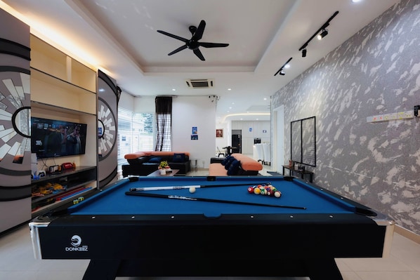 Une table de billard avec une queue de billard, des billes et un porte-billes, dans une pièce moderne dotée d’un ventilateur de plafond, d’un éclairage encastré et d’un grand écran de télévision.