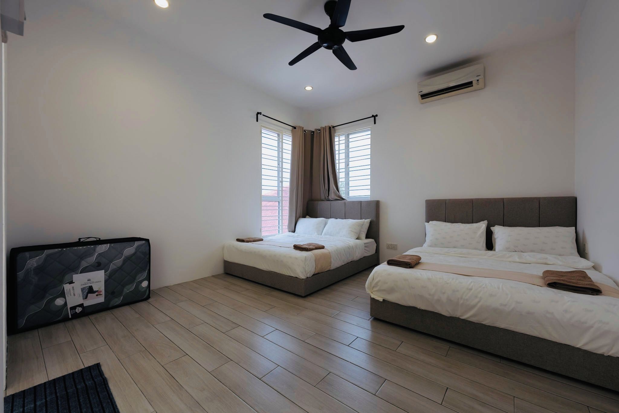 Habitación de hotel con dos camas, ventilador de techo, aire acondicionado y una maleta en el suelo.