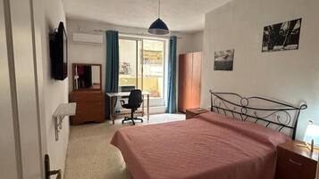 A bedroom with a bed, a desk, a chair, a wardrobe, and a television on the wall.