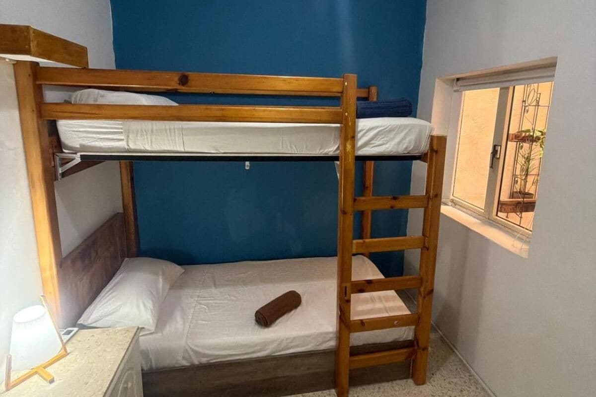 Quarto com beliche, janela e escrivaninha.