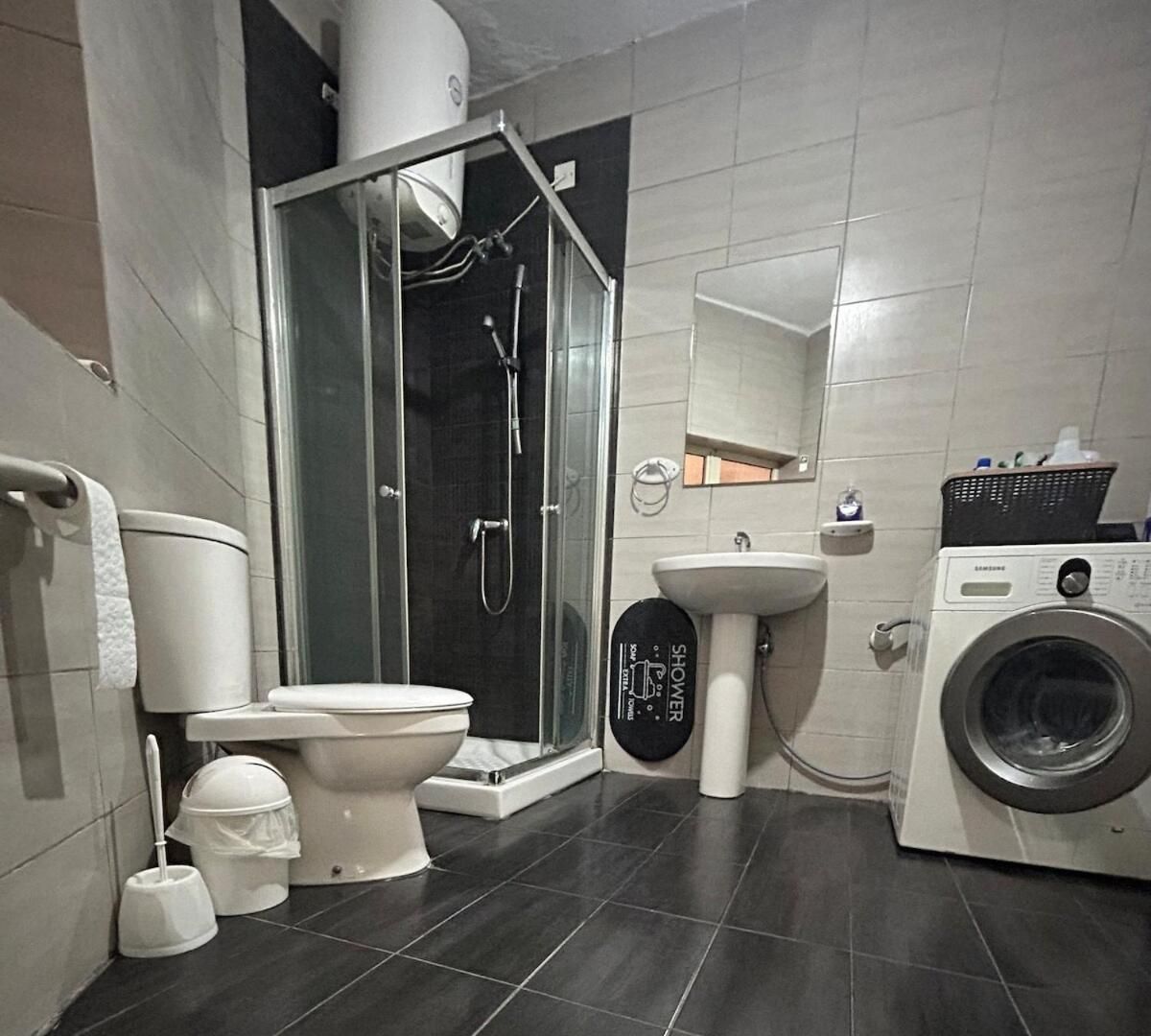 A modern bathroom with a toilet, shower, sink, and washing machine.