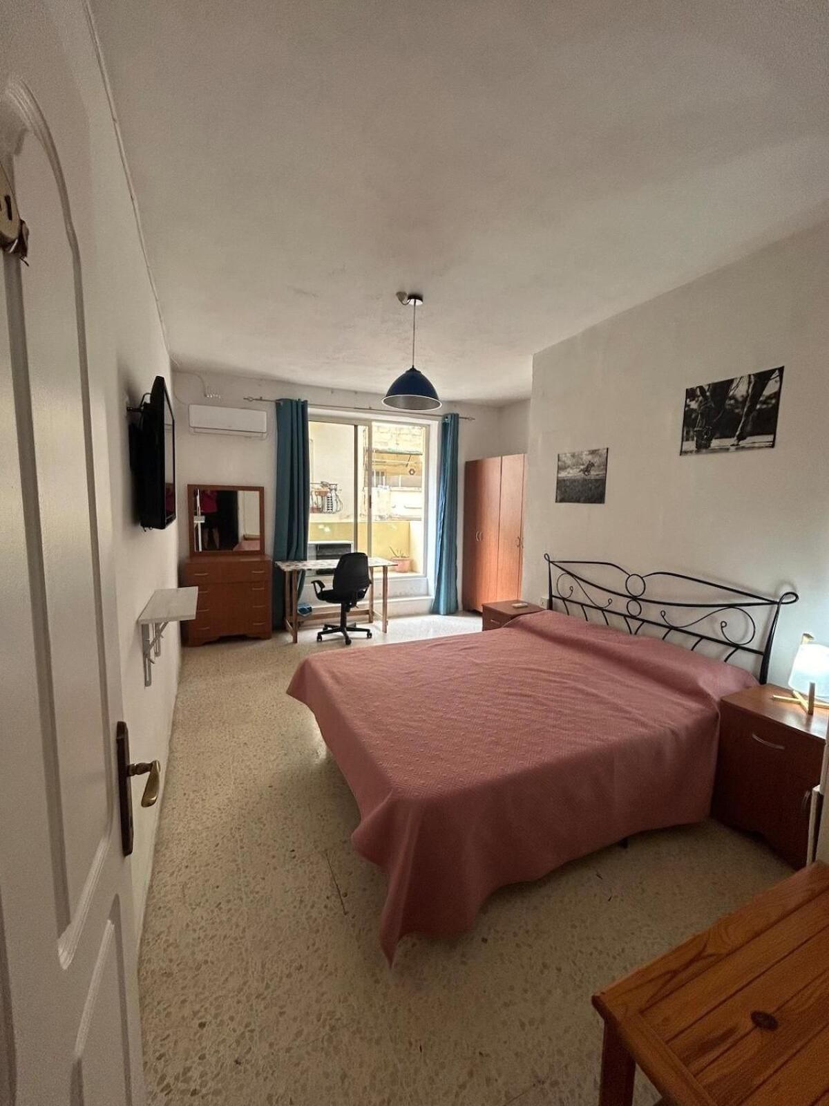 A bedroom with a bed, a desk, a chair, a wardrobe, and a television on the wall.