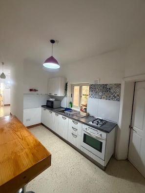 Cozinha compacta com armários brancos, uma mesa de jantar de madeira, fogão a gás e luminária pendente.