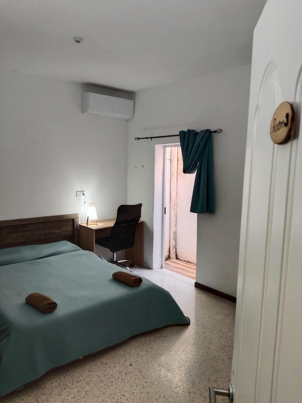 Ett hotellrum med en säng, ett skrivbord, en stol och ett fönster med gardiner.