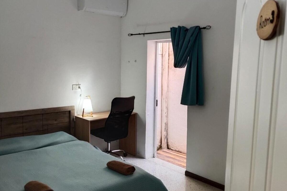 Quarto de hotel com cama, escrivaninha, cadeira e janela com cortinas.