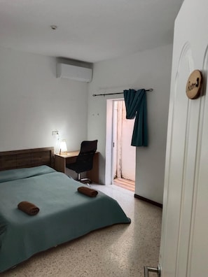Quarto de hotel com cama, escrivaninha, cadeira e janela com cortinas.
