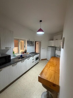 A kitchen with white cabinets, a wooden countertop, a sink, a stove, and a hanging pendant light.