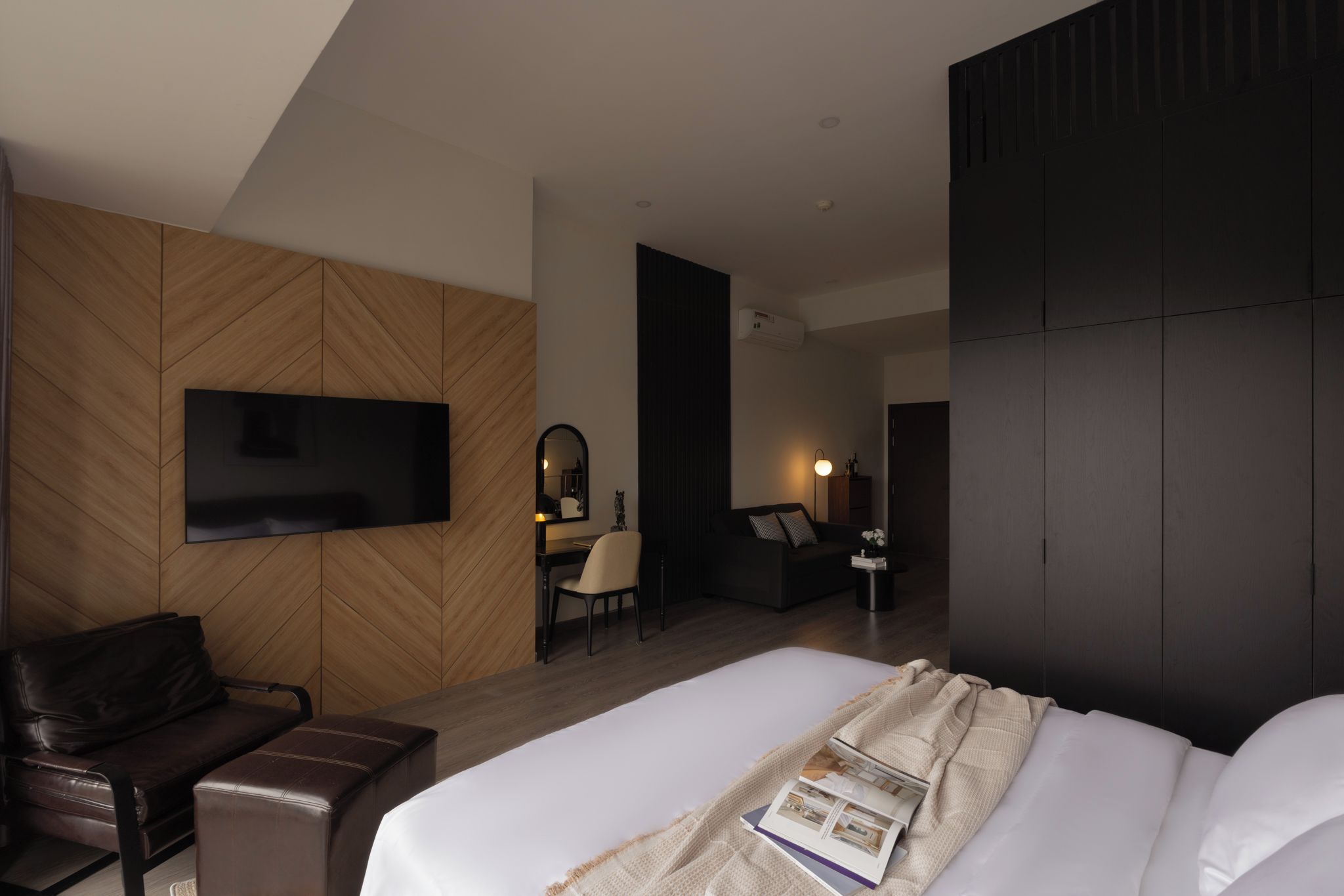 Camera d'albergo moderna con un letto grande, una TV a schermo piatto montata a parete, una scrivania con una sedia e un armadio di colore scuro.