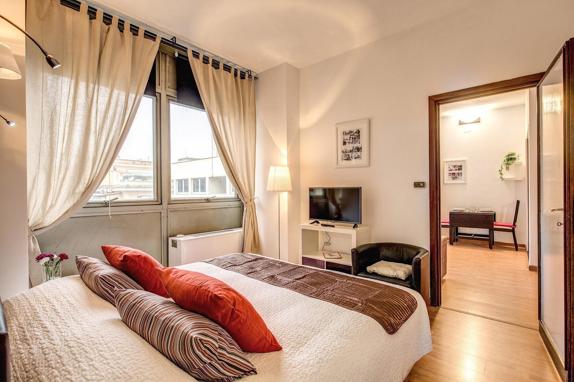 A hotel room with a bed, a TV, a desk, and a dining area.