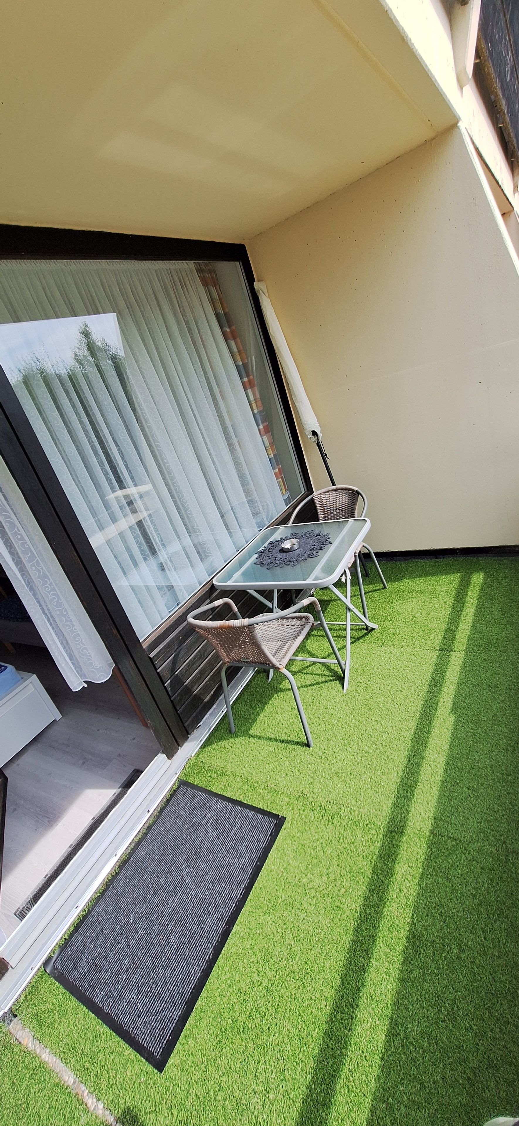 Een balkon met kunstgras, een tafel en twee stoelen.