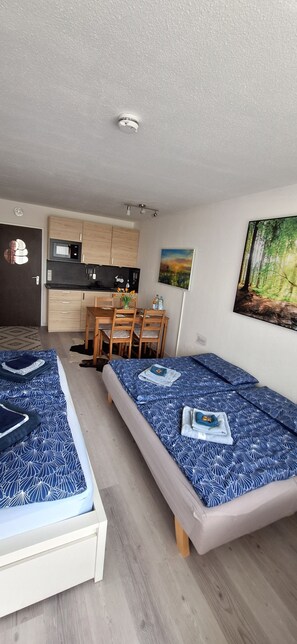 Ein kompaktes Zimmer mit zwei Betten, einer Küchenzeile, einem Essbereich und einem Bild an der Wand.