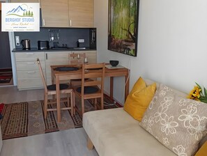 Un espacio habitable compacto con kitchenette, zona de comedor y sofá con cojines estampados.