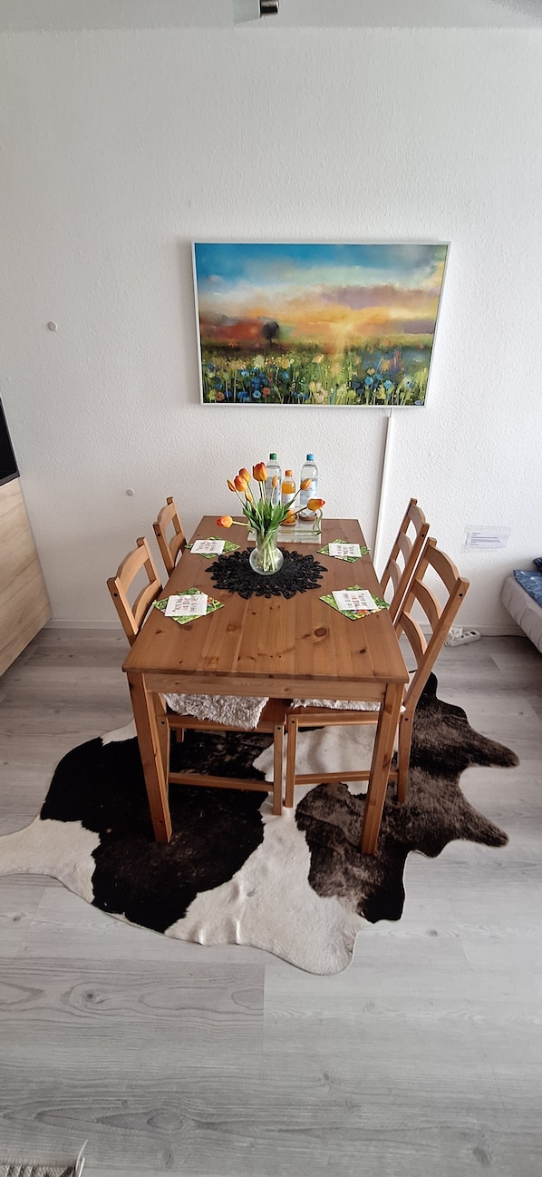 Ein Esstisch mit Stühlen, eine Vase mit Blumen und ein Gemälde an der Wand.
