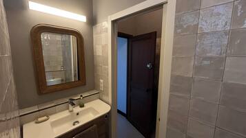 Een badkamer met een spiegel, wastafel en een deur naar een andere kamer.