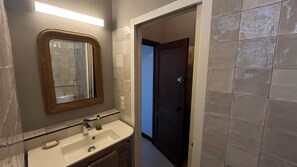 Een badkamer met een spiegel, wastafel en een deur naar een andere kamer.