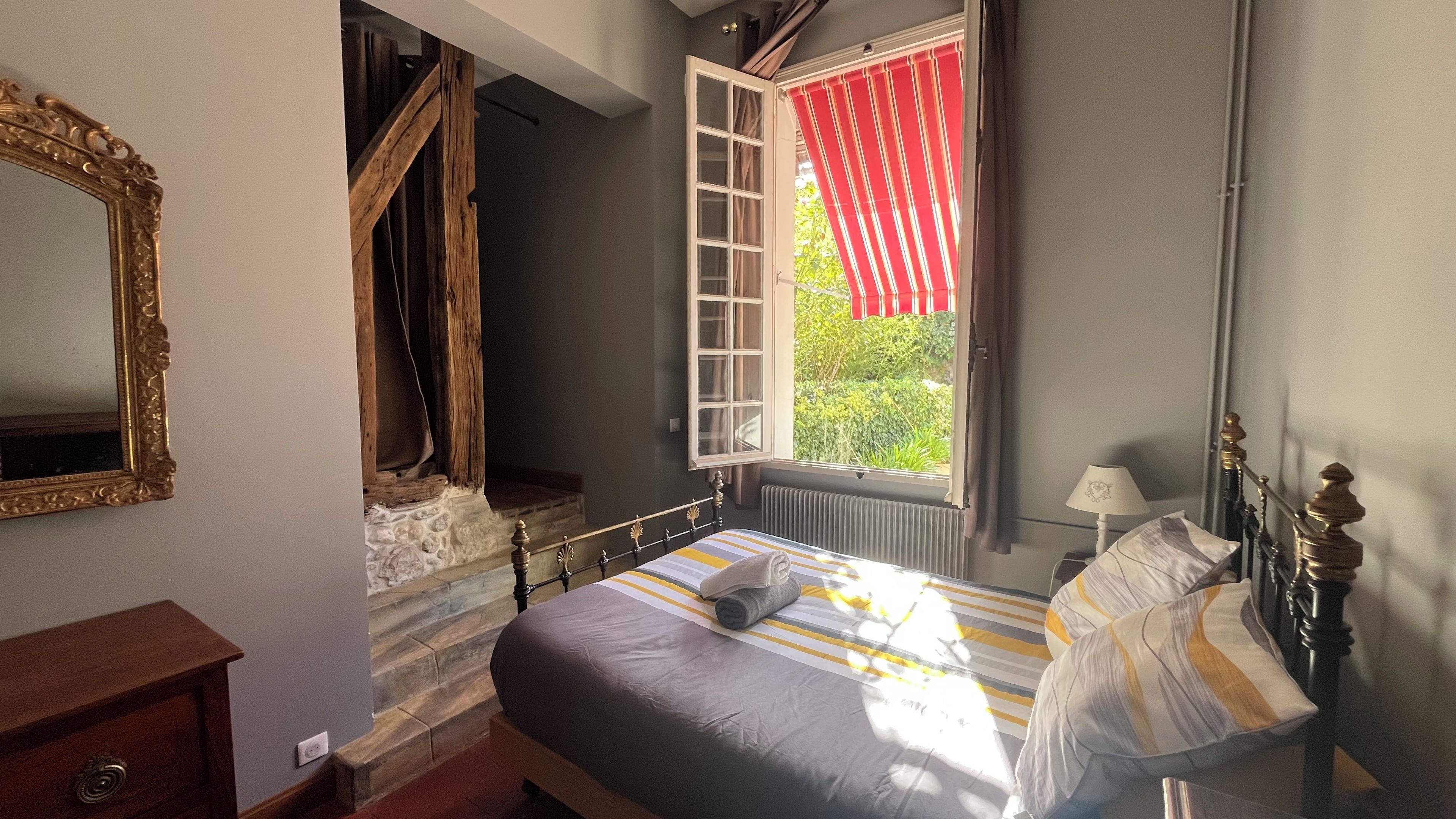 Een slaapkamer met een bed, een raam met rode gordijnen, een houten trap en een spiegel.