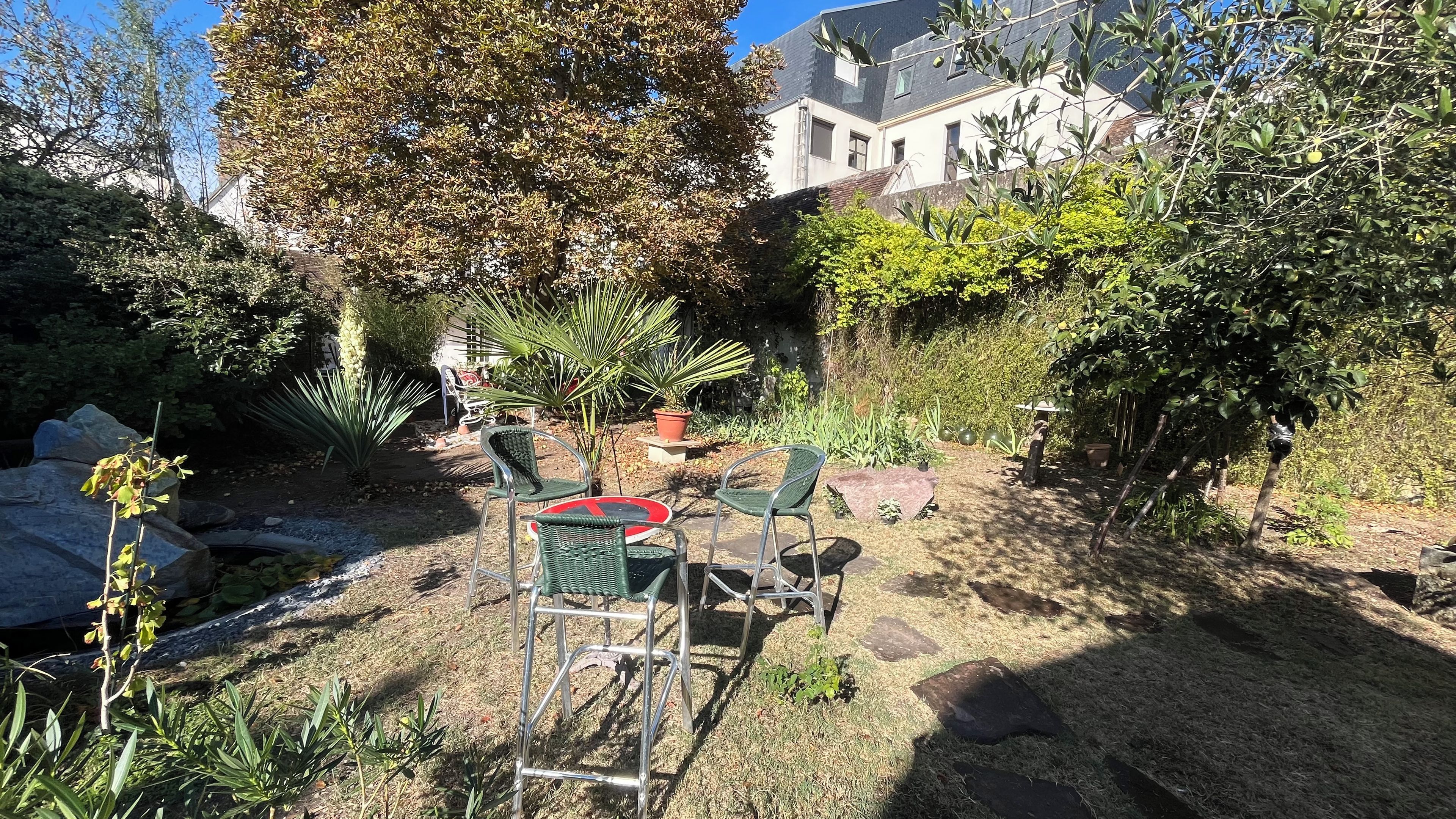 Een terras met stoelen en een tafel, omringd door diverse planten en bomen.