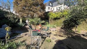 An outdoor seating area with chairs and a table, surrounded by various plants and trees. - New Listing (Sens)