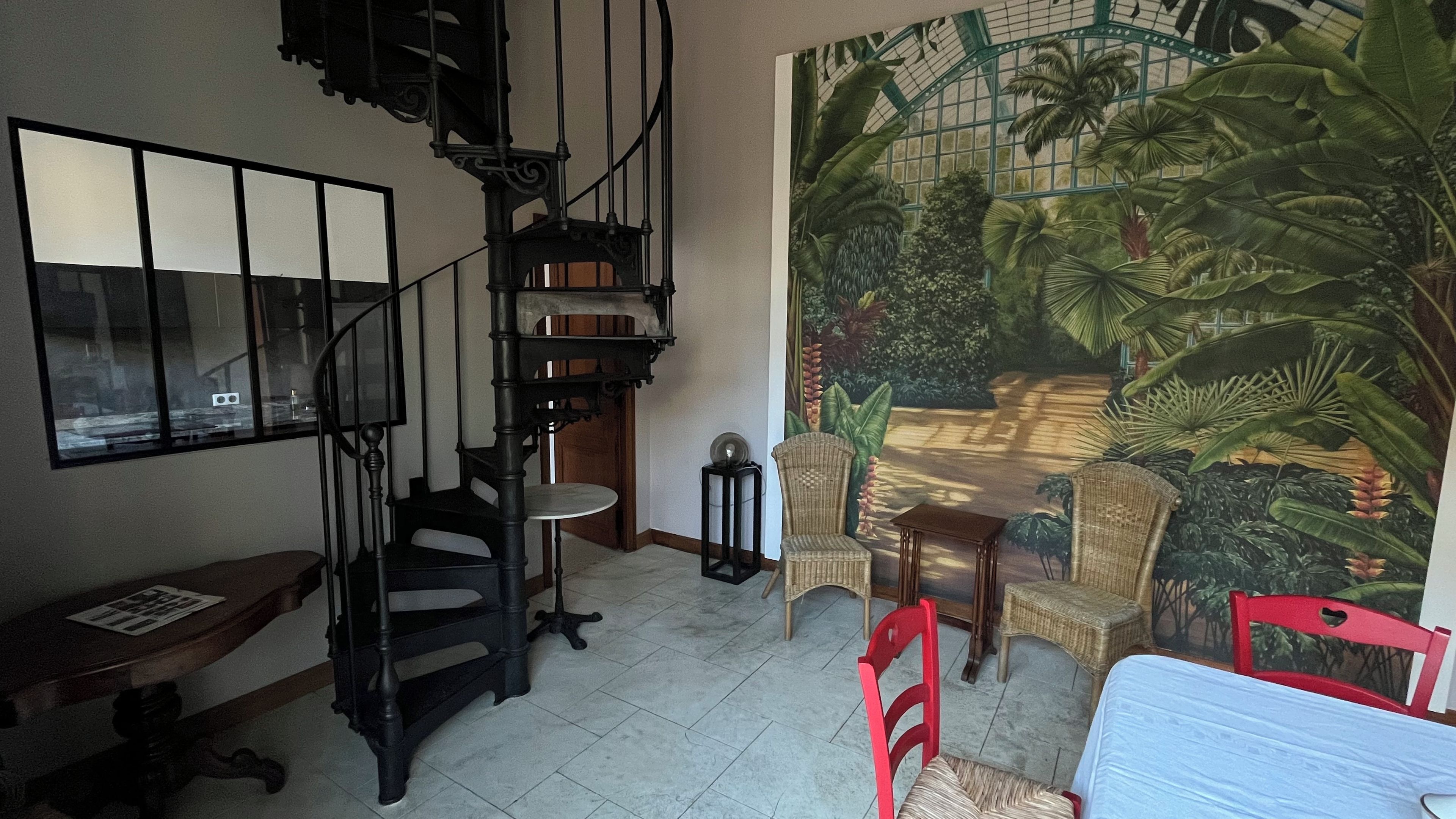 A room with a spiral staircase, a large tropical mural, wicker furniture, and a bed.