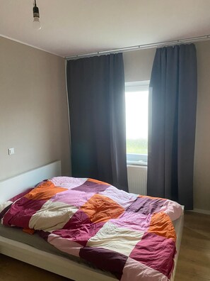 Una cama individual con un edredón colorido, una ventana con cortinas oscuras y una lámpara en el techo.