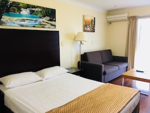 A hotel room with a bed, a sofa, a desk, and a lamp. - Centenary Motor Inn (Darra)