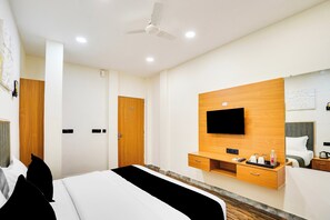 Quarto de hotel com uma cama, televisão na parede, ventoinha no teto e cómoda de madeira.
