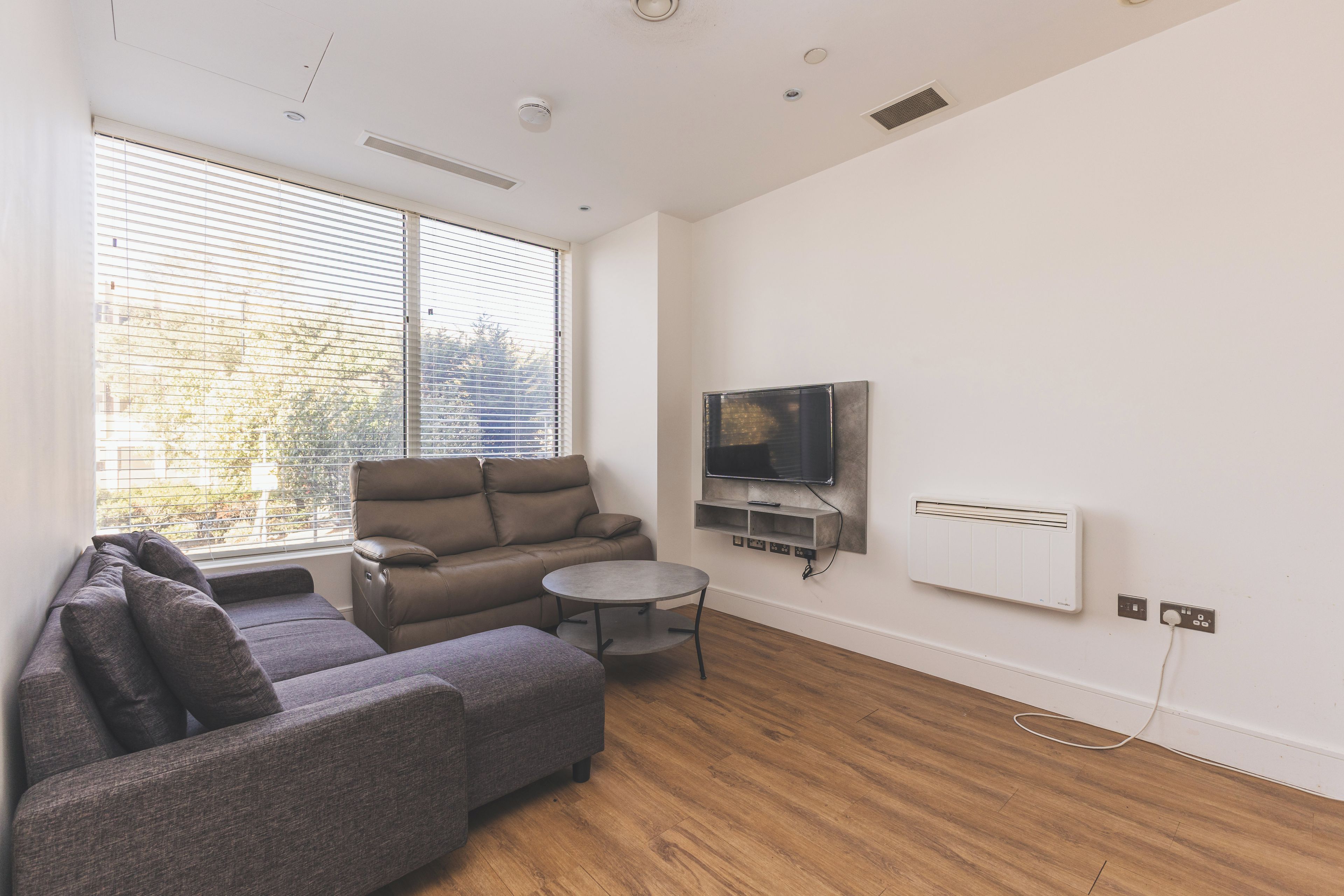 A modern living room with a sofa, a smaller couch, a coffee table, a flat-screen TV, and a built-in air conditioning unit.