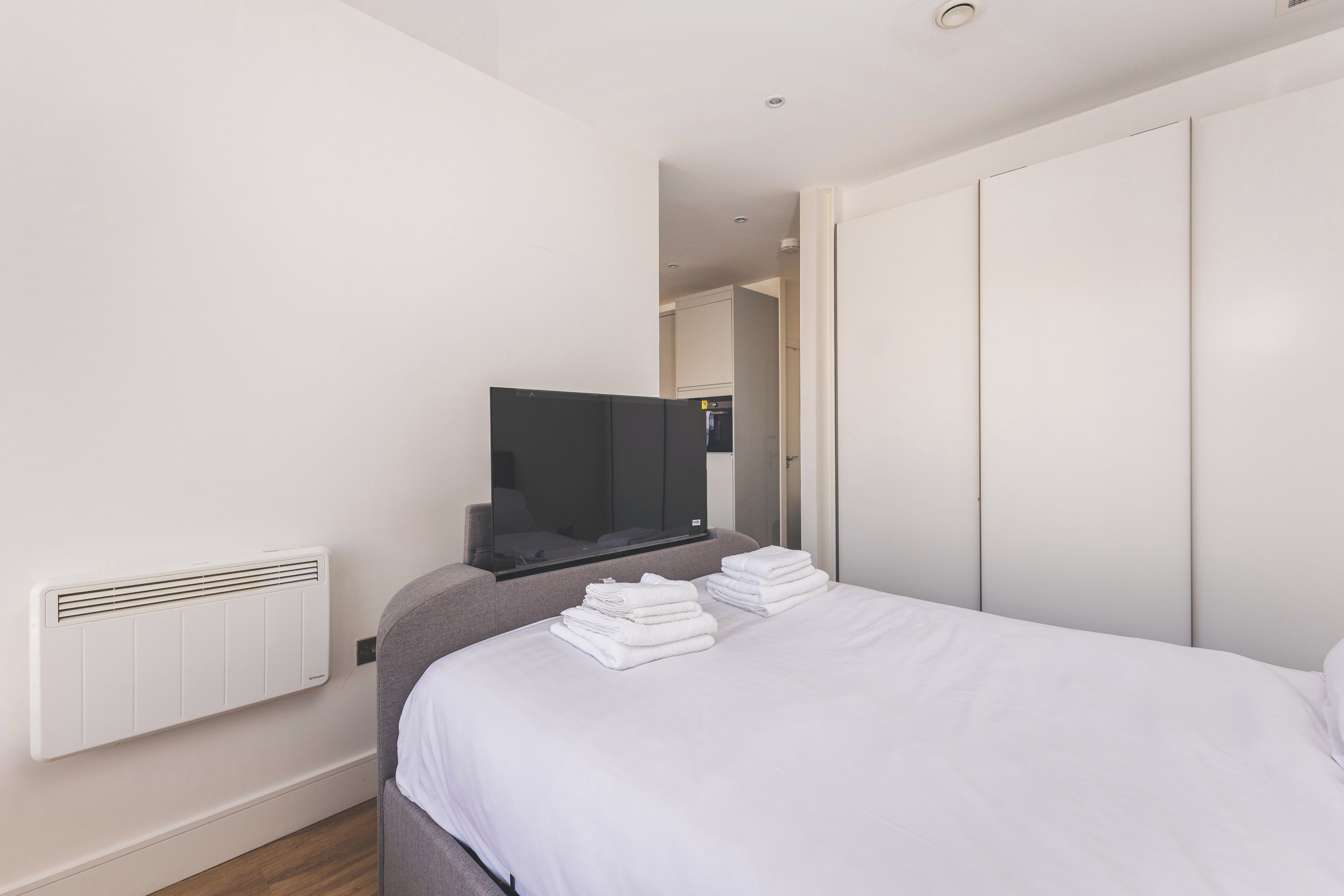 A hotel room with a bed, a television, a radiator, and a wardrobe.
