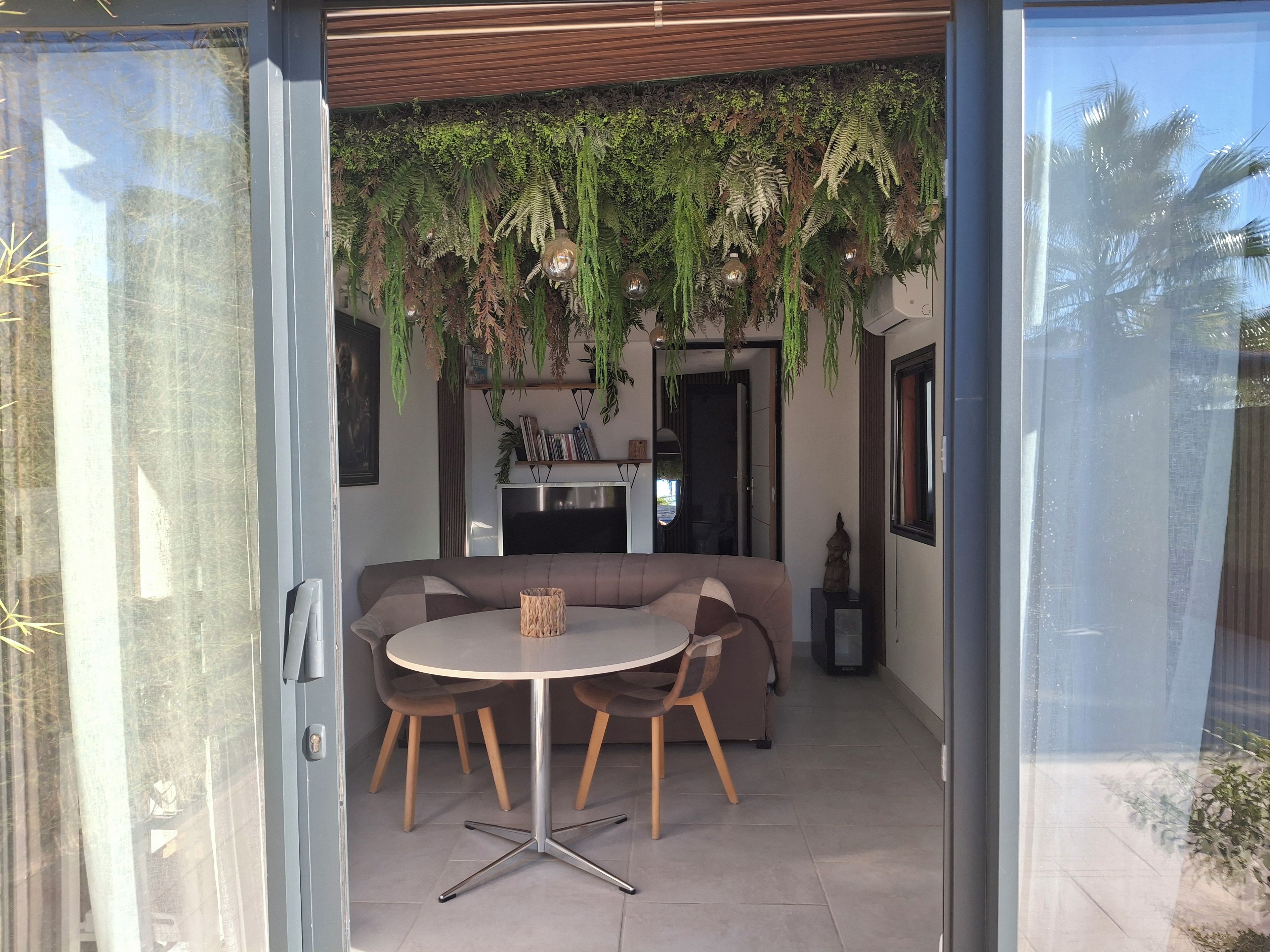 An open-plan living space with a dining area, a sofa, and hanging plants.