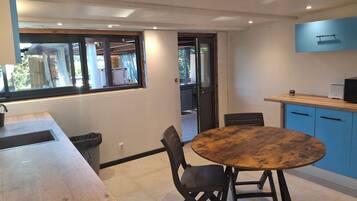 A dining area with a wooden table and chairs, a window with a view, and a kitchen area with blue cabinets and a microwave.
