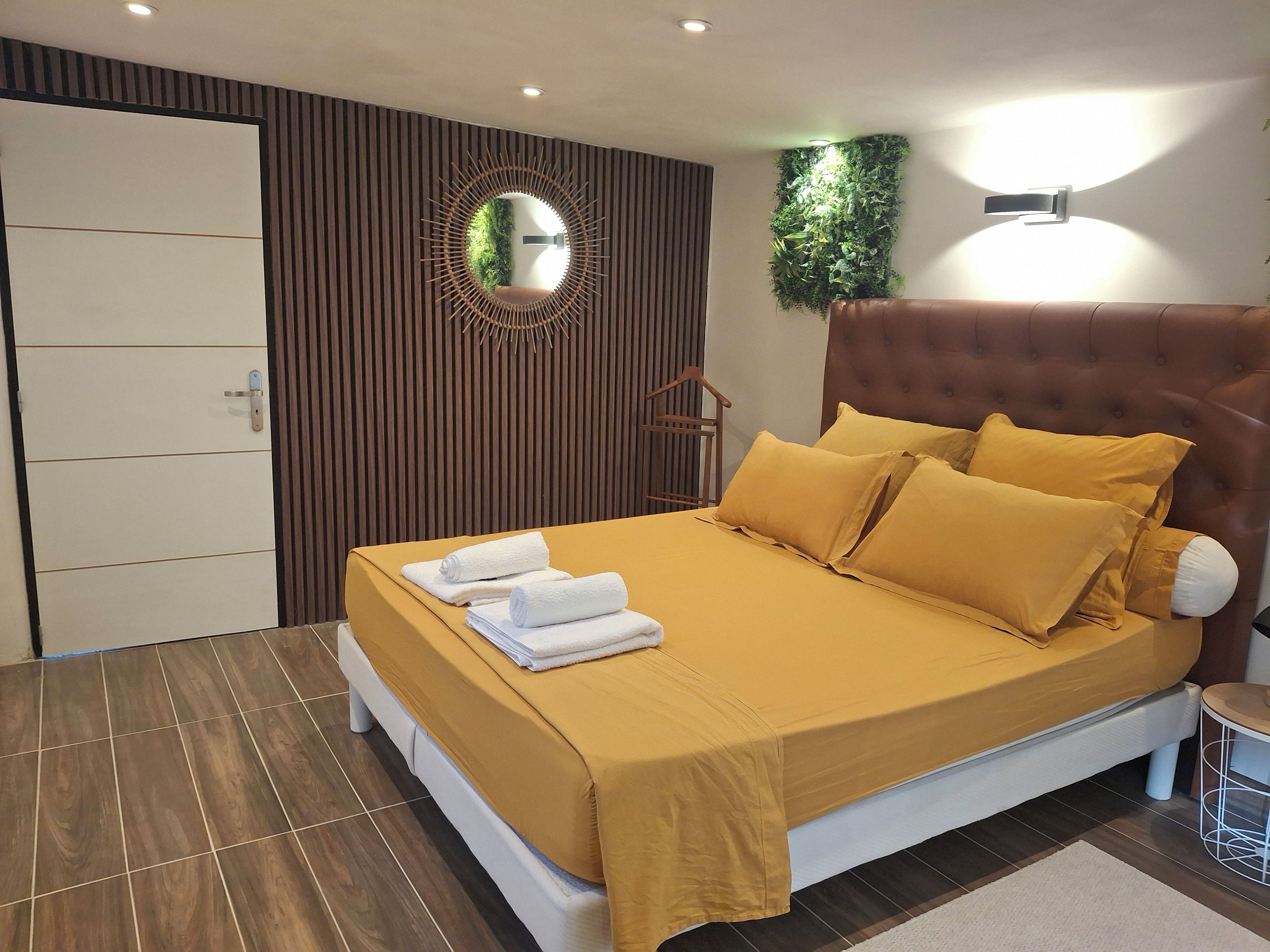 Une chambre moderne avec un grand lit, un miroir, une lampe fixée au mur et une porte dotée d’une poignée.