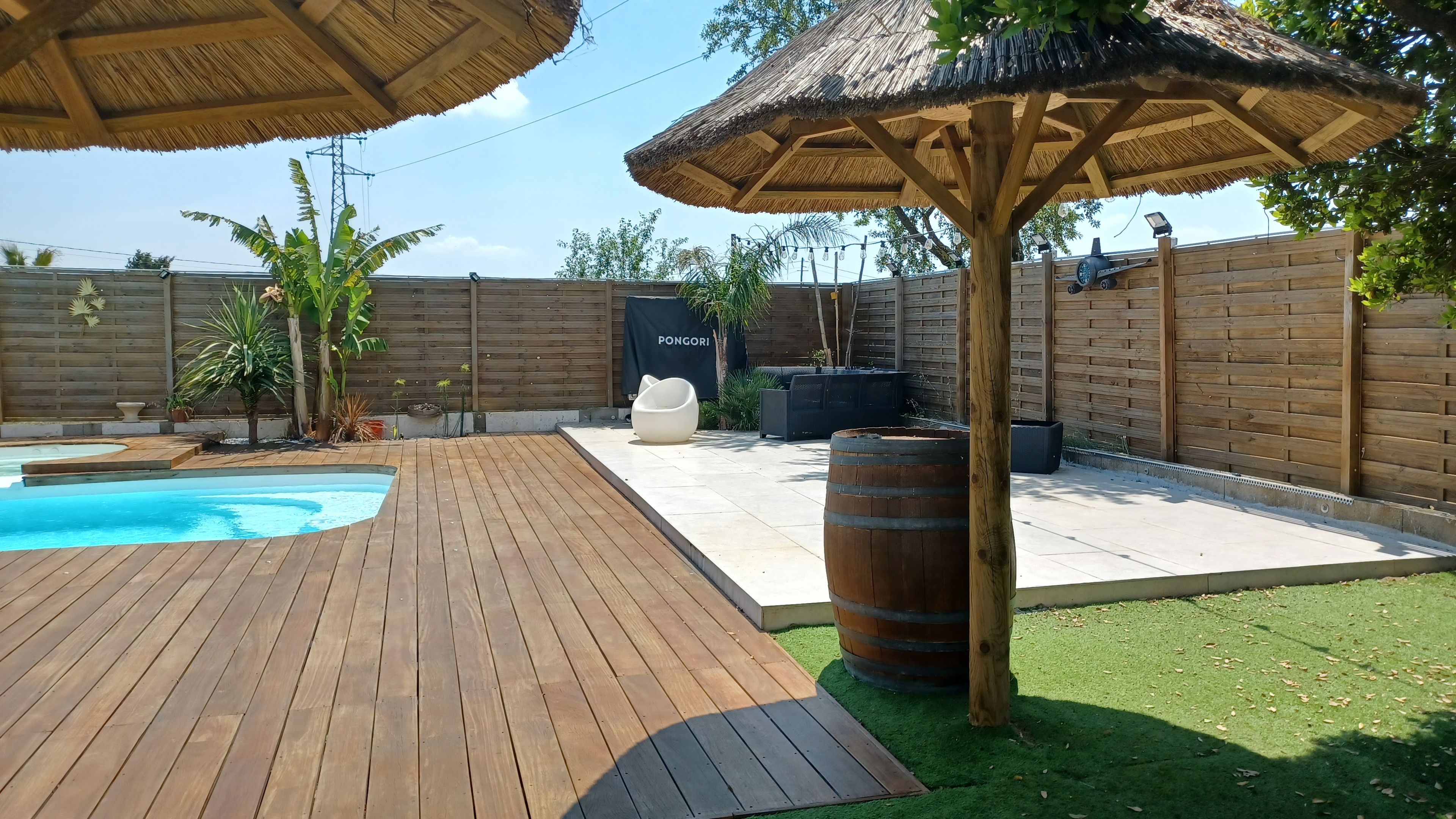 A backyard with a wooden deck, a swimming pool, a barbecue area, and a covered seating space.