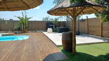 A backyard with a wooden deck, a swimming pool, a barbecue area, and a covered seating space.