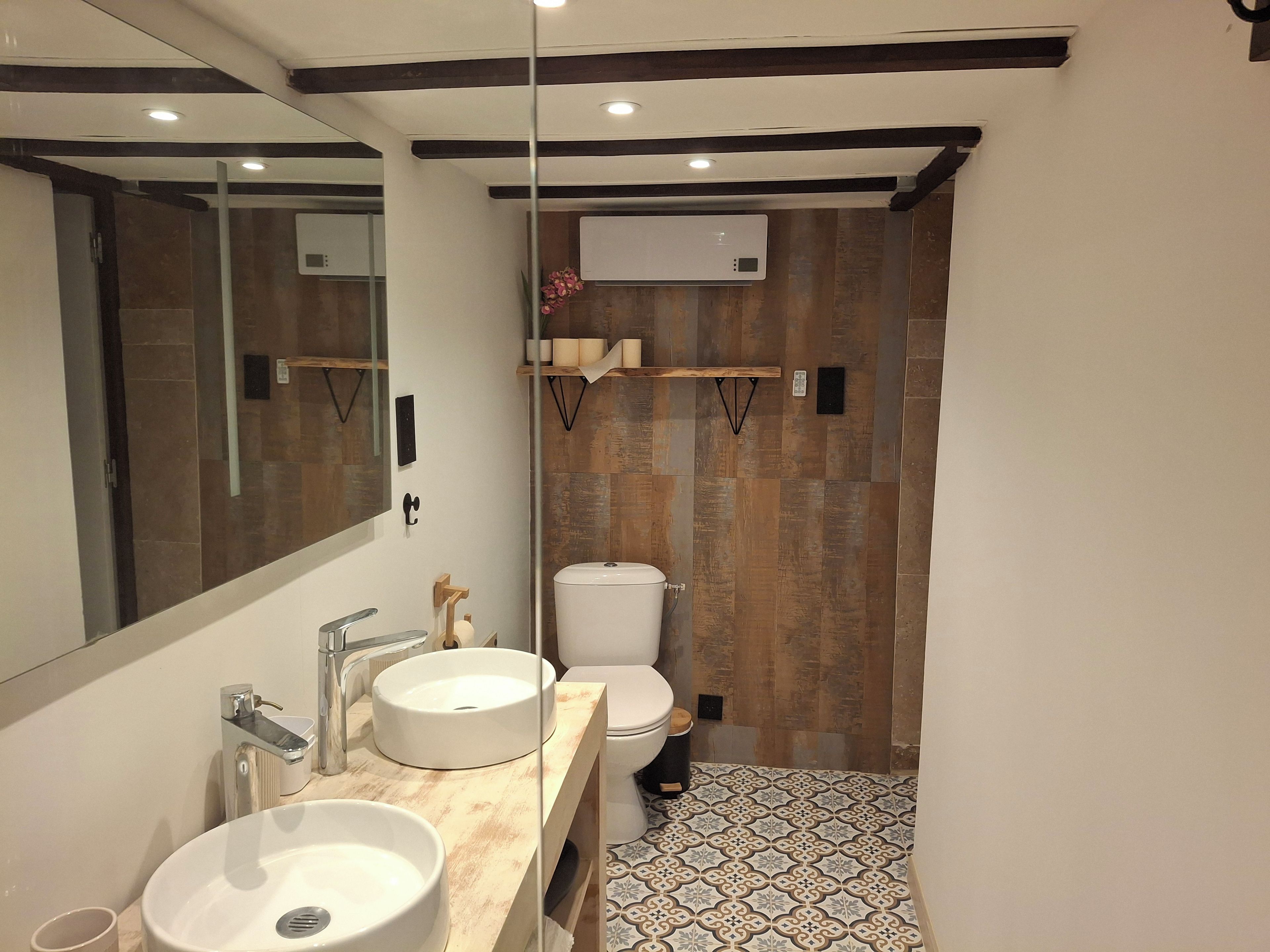 A modern bathroom with a large mirror, two sinks, a toilet, and a shower area.