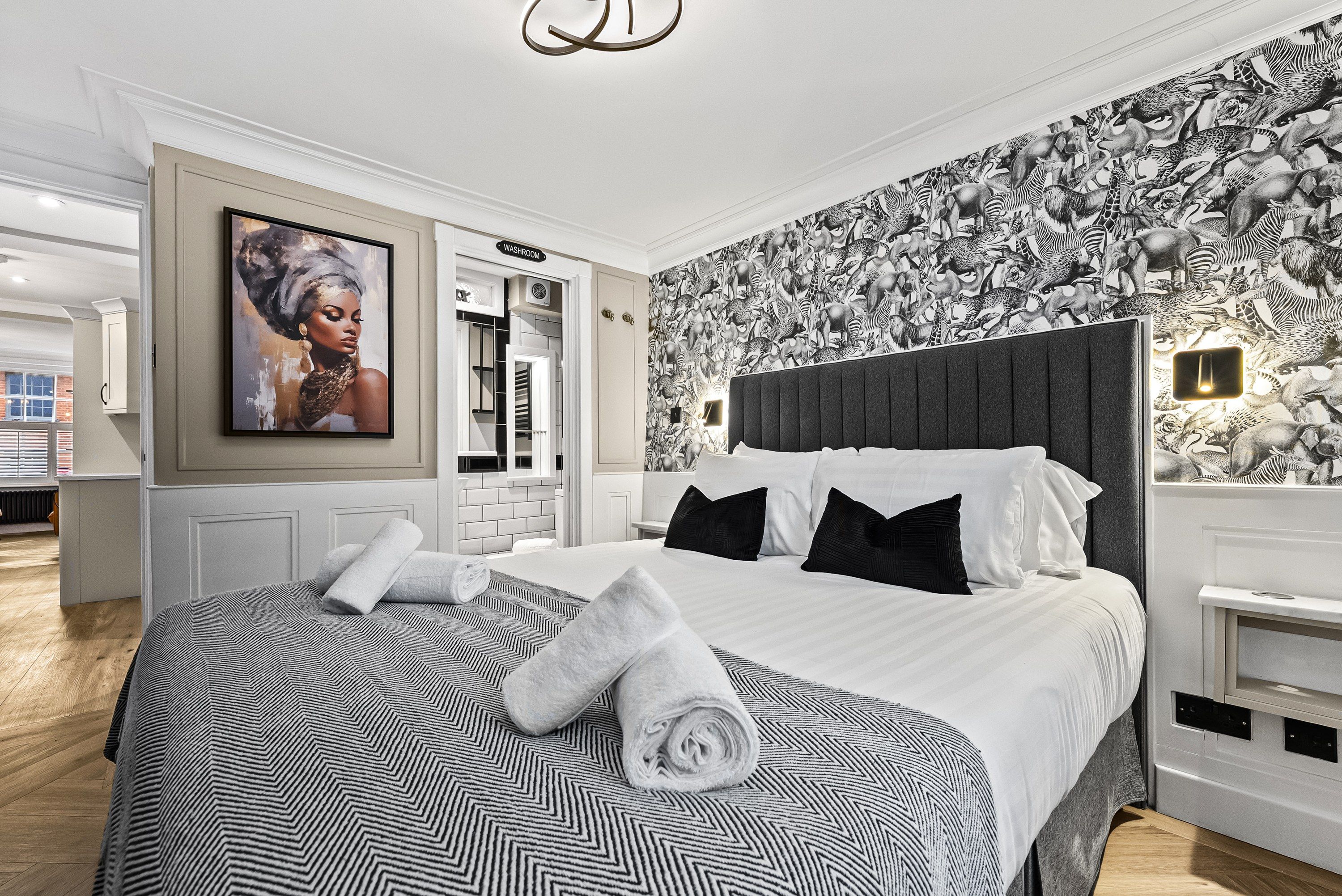 A modern bedroom with a large bed, a patterned wall, and a painting.