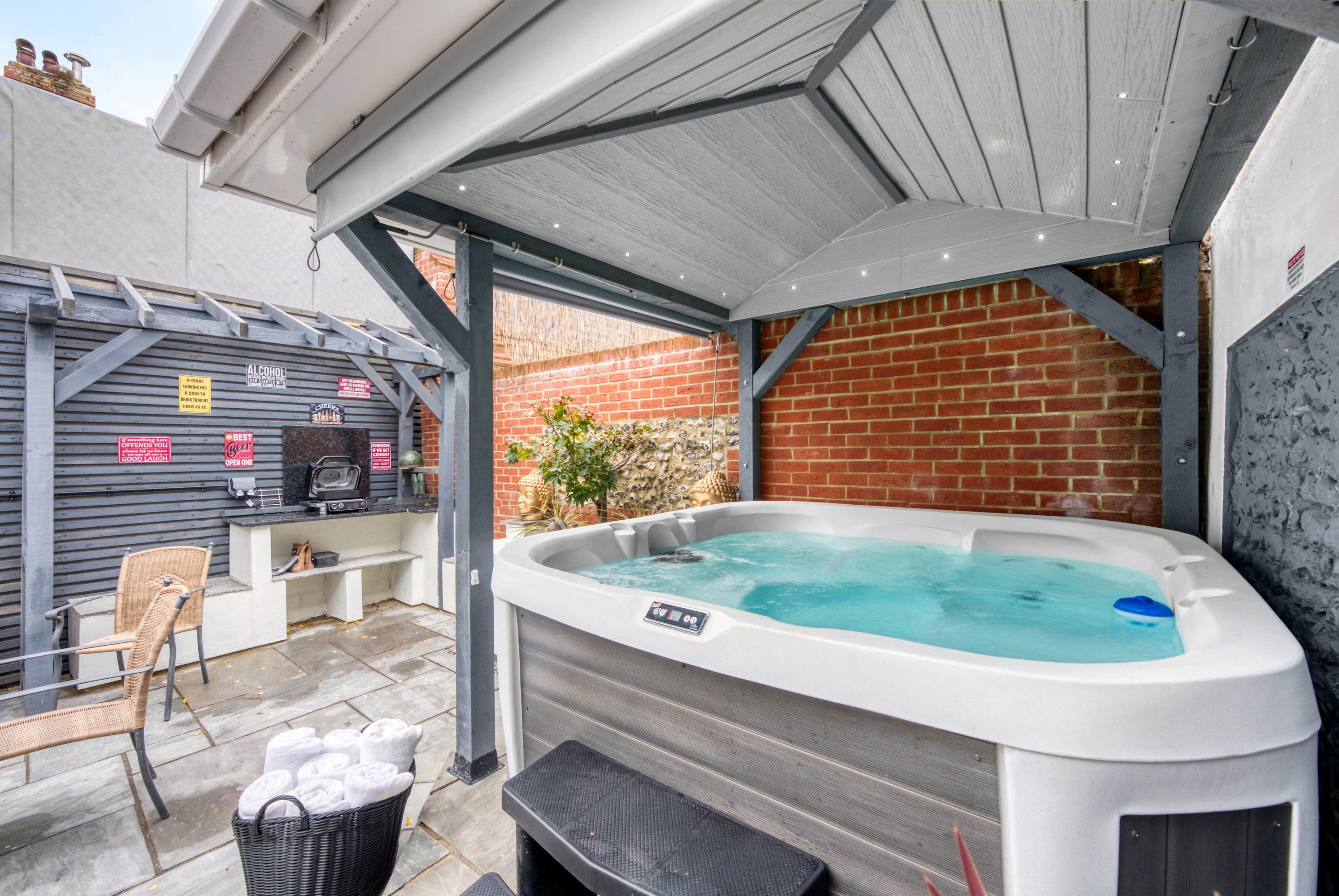 Ein Whirlpool in einem überdachten Außenbereich mit Backsteinwand und Grillstation.