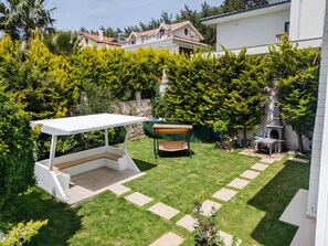 Un patio trasero con terraza, una parrilla y un pequeño jardín.