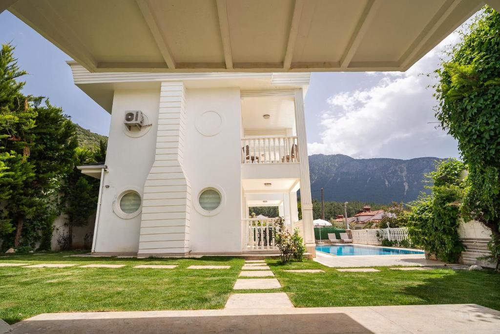 A two-story house with a covered porch, a swimming pool, and a mountainous backdrop.